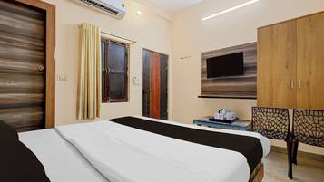 A hotel room with a bed, a TV mounted on the wall, a wooden wardrobe, and a small table with a kettle and cups.