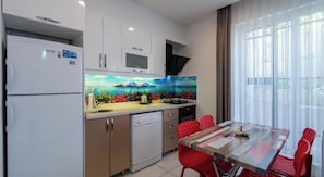 Cocina compacta con refrigerador, microondas y lavavajillas. Una mesa de comedor con sillas rojas y vistas amplias por grandes ventanales.