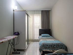Une chambre à coucher comprenant un lit, un bureau avec une planche à repasser, une armoire et une fenêtre avec des rideaux.