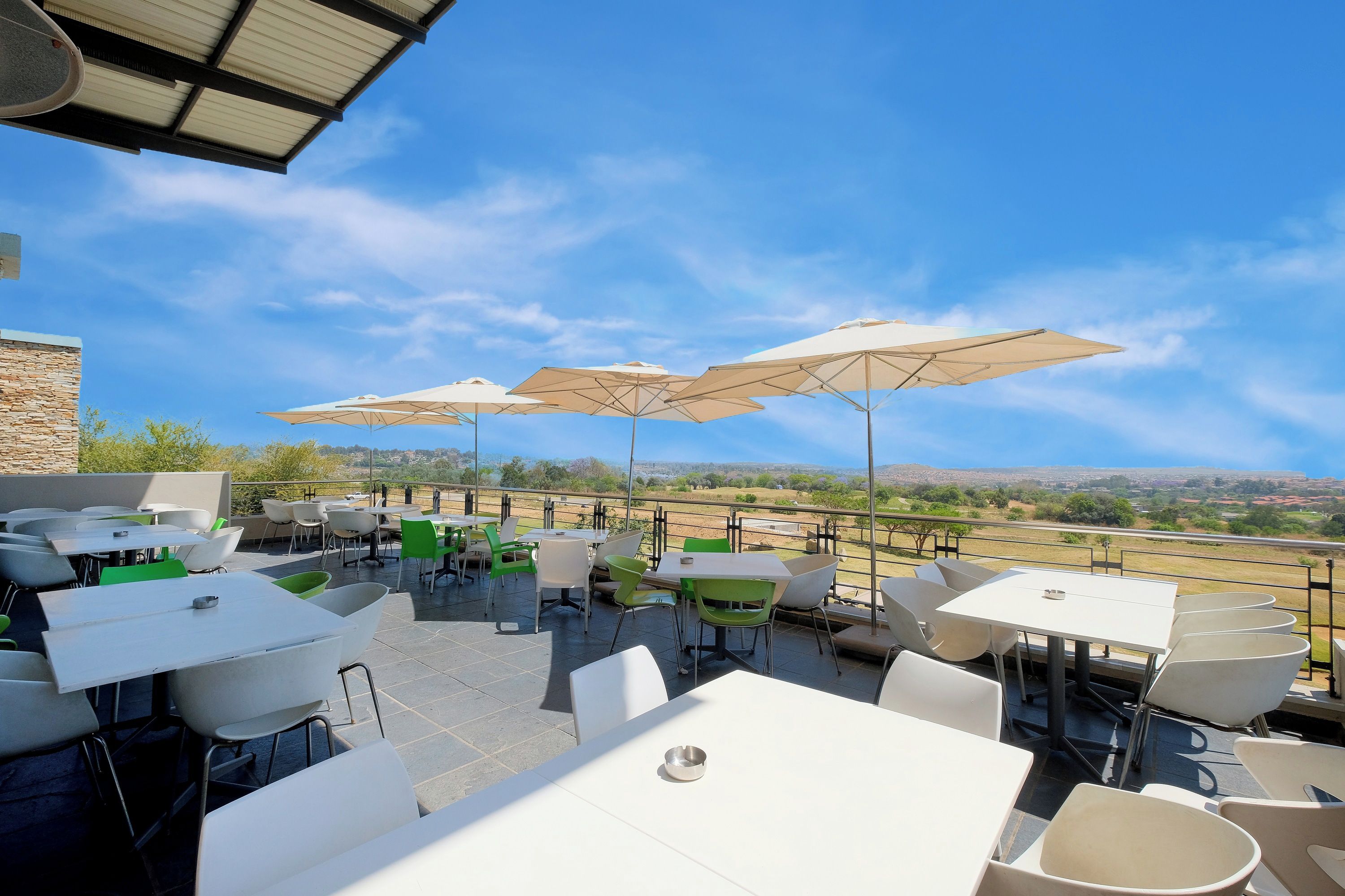 Eine Terrasse im Freien mit Tischen, Stühlen und Sonnenschirmen, mit Blick auf die Landschaft.
