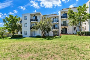 A modern apartment building with multiple balconies, a well-maintained lawn, and mature trees. - Tee Off & Unwind at Jackal Creek by ctha (Roodepoort)