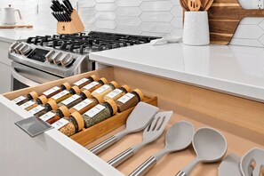 Een keuken met een roestvrijstalen fornuis, een lade met kruidenpotjes en keukengerei.