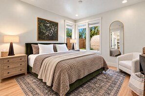 A bedroom with a bed, bedside tables, a mirror, and a window with a view of greenery. - Luxury Eagle Getaway | Private Barrel Sauna, Climate-Controlled Game Room & Outdoor Fire Pit (Eagle)