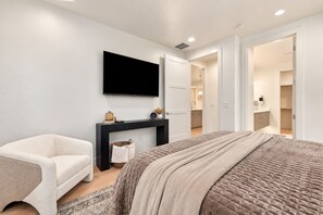 Een moderne slaapkamer met een bed, een stoel, een televisie en een console tafel.