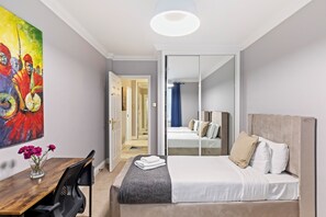 Ett hotellrum med en säng, ett skrivbord, en stol, en tavla och en spegel.