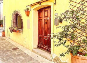 A yellow building with a wooden door and a window with metal bars. - La Cicala - Charm & Relaxation Just 5 Minutes from the Sea (Rosignano Marittimo)