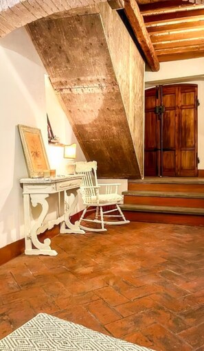 A rustic interior with a sloped ceiling, wooden flooring, a rocking chair, a desk with a lamp, and a wooden door. - La Cicala - Charm & Relaxation Just 5 Minutes from the Sea (Rosignano Marittimo)