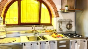 A kitchen with a double sink, stainless steel appliances, a gas stove, and a brick arch window. - La Cicala - Charm & Relaxation Just 5 Minutes from the Sea (Rosignano Marittimo)