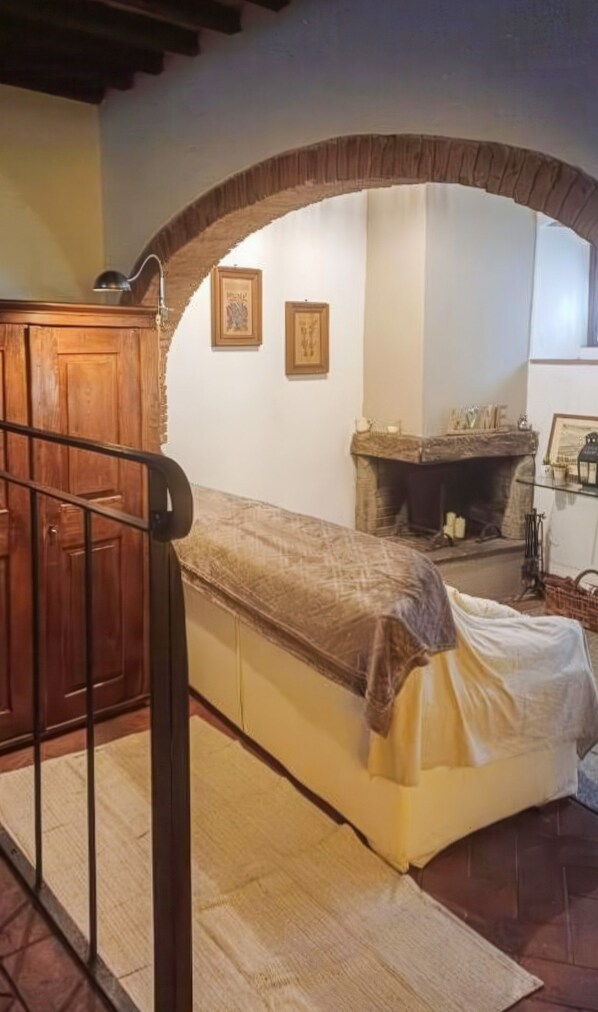 A room with a bed, wooden cabinet, fireplace, and framed pictures on the wall. - La Cicala - Charm & Relaxation Just 5 Minutes from the Sea (Rosignano Marittimo)