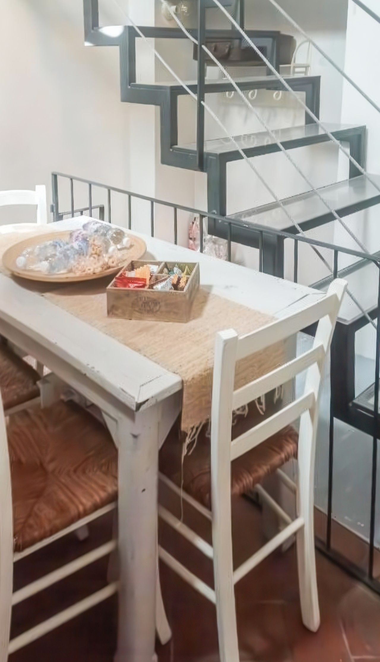 Un coin repas avec une table dressée pour deux personnes, une boîte de chocolats et une vue sur un escalier moderne.