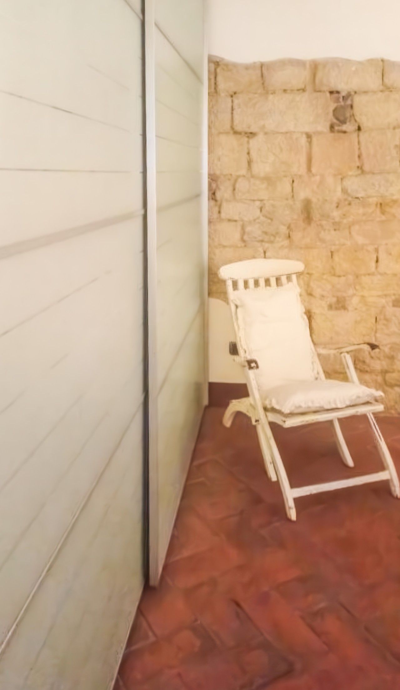 Una habitación con pared de piedra, una silla blanca y piso estampado.