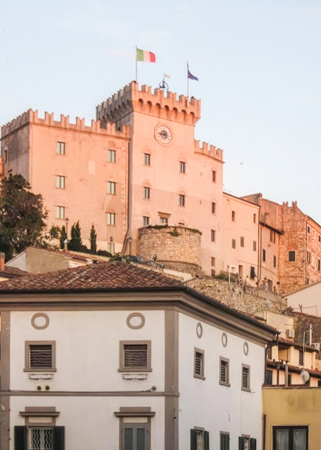 Un edificio histórico con una torre destacada que tiene un reloj y banderas, rodeado de otros edificios con arquitectura tradicional.