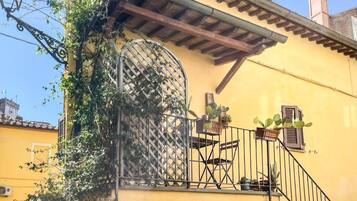 A yellow building with a balcony, a wrought iron gate, and a small table with potted plants.