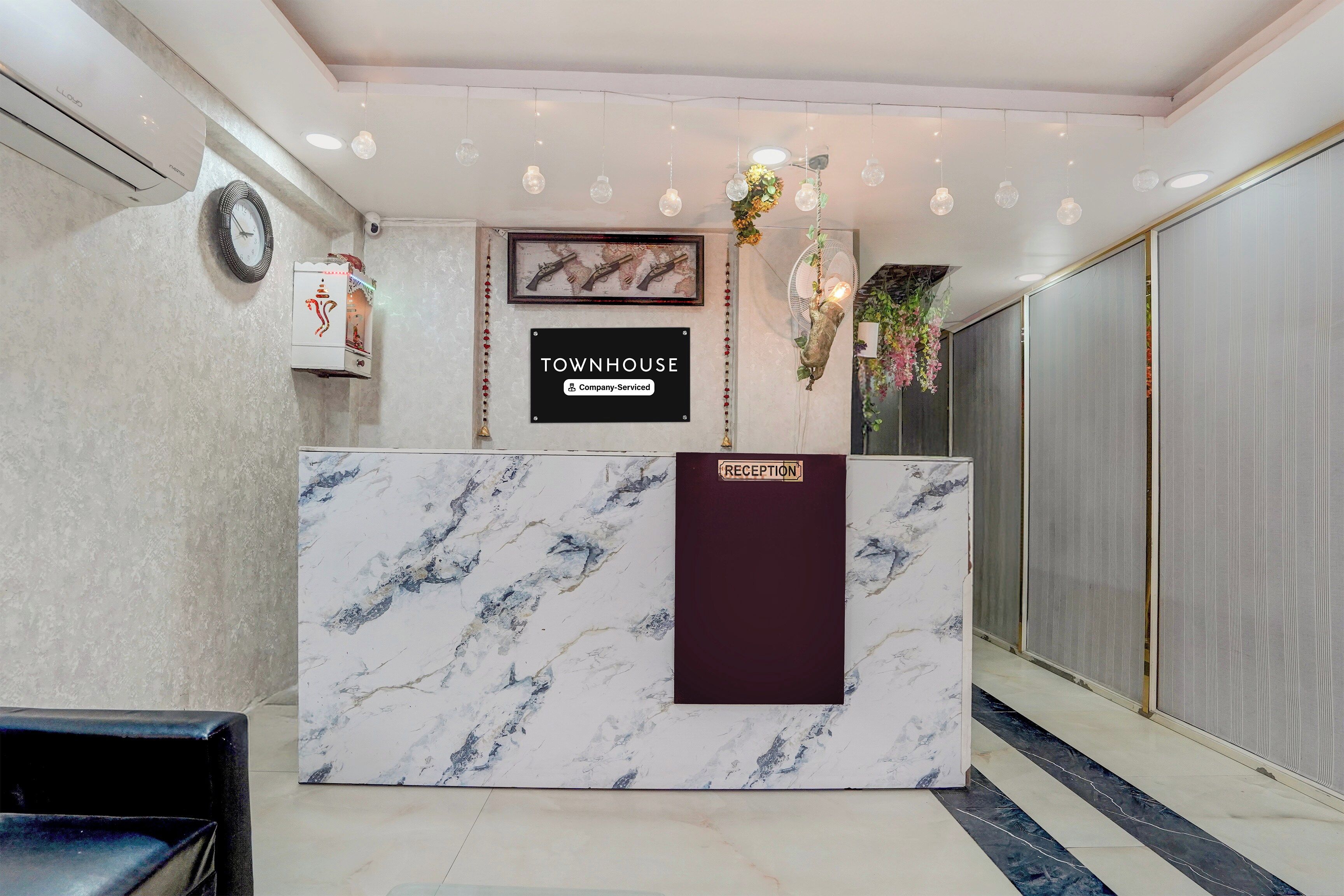 A reception desk with a marble top, a sign indicating it's a company-serviced townhouse, and a reception area with a fan and decorative plants.
