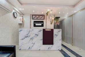 A reception desk with a marble top, a sign indicating it's a company-serviced townhouse, and a reception area with a fan and decorative plants. - Townhouse Jagannath Temple Noida (Noida)