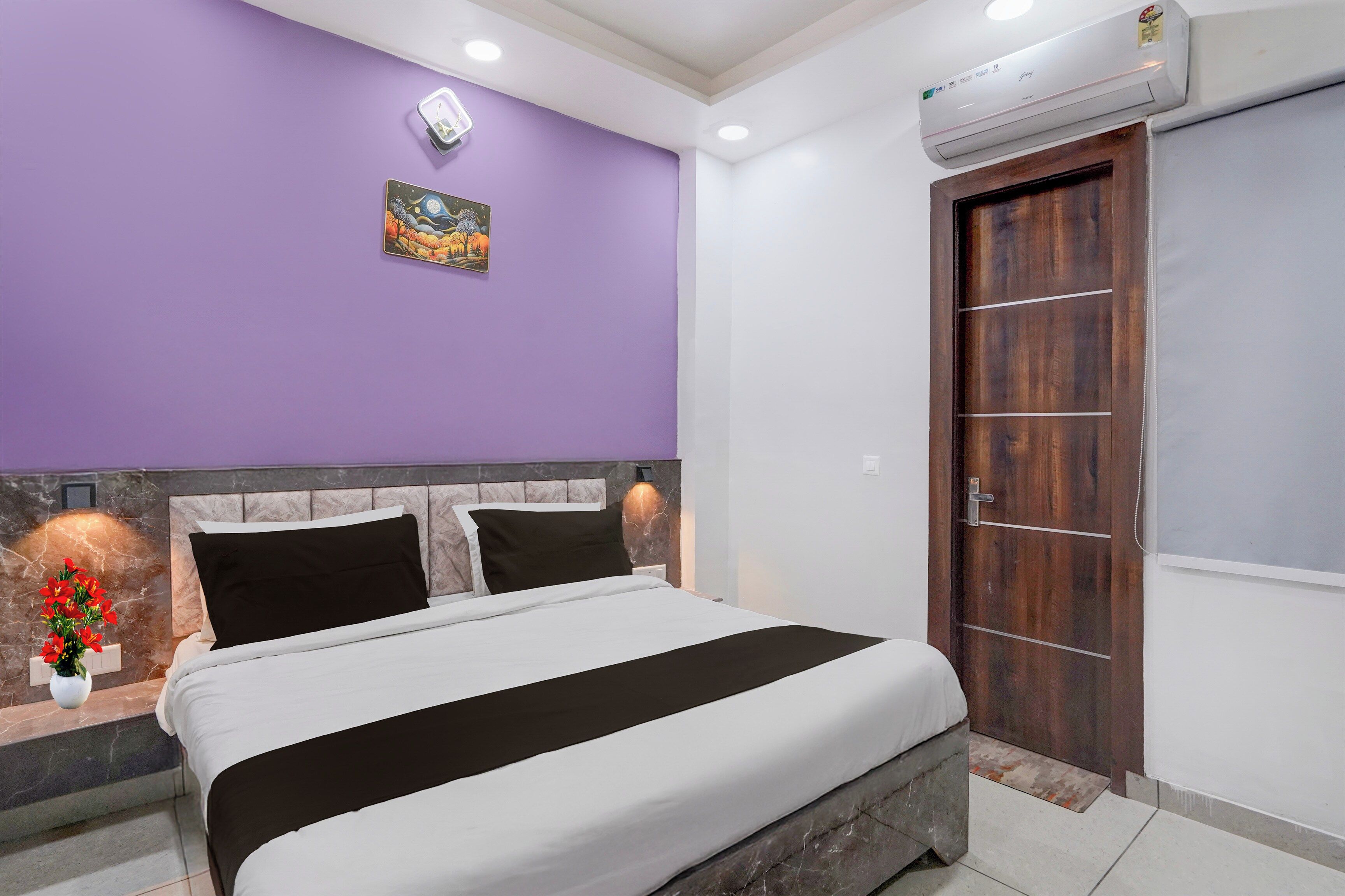 A bedroom with a bed, a wall-mounted air conditioner, a door, and a small wall decoration.