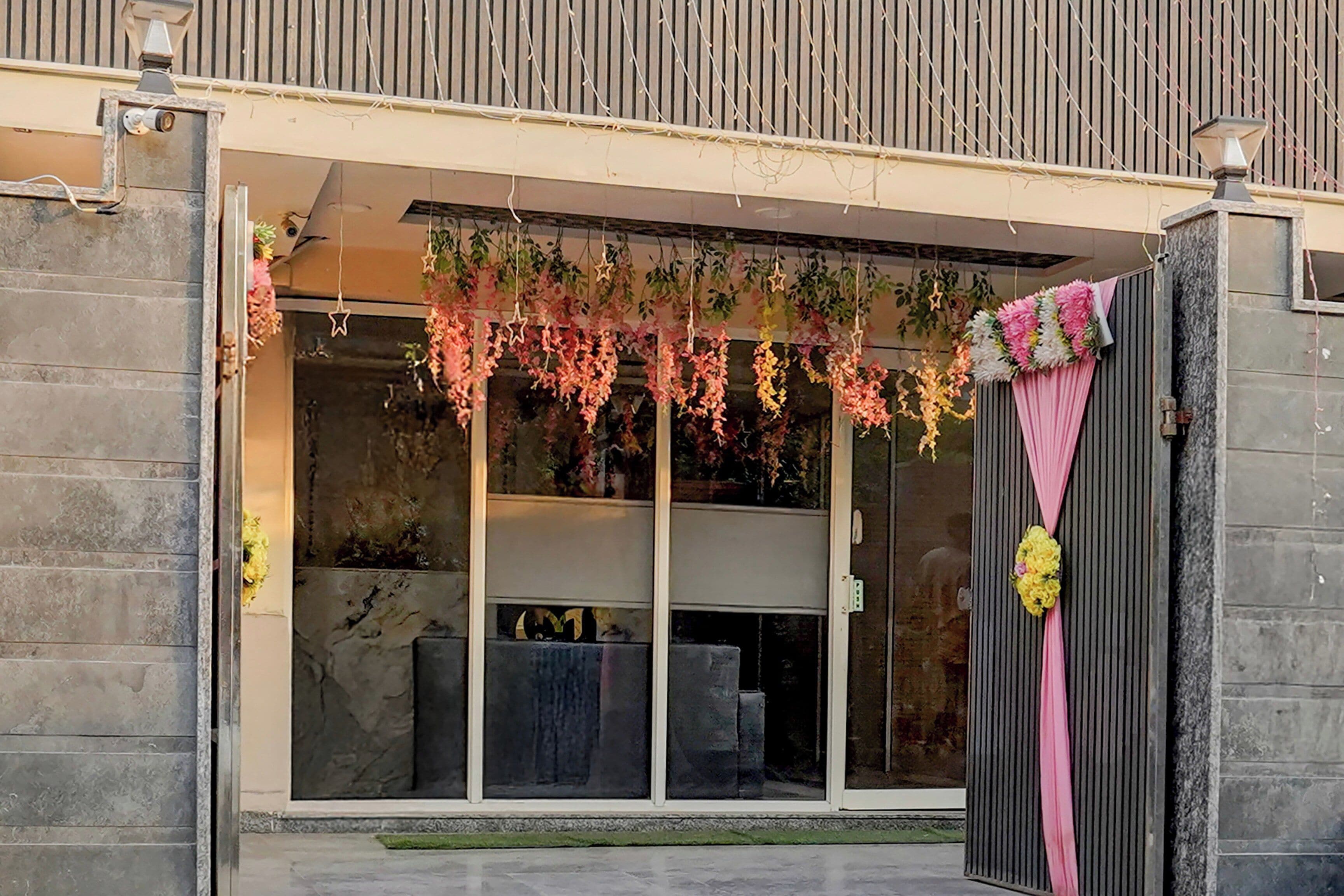 A modern building with a glass door entrance, a stone facade, and a small outdoor seating area visible through the glass.