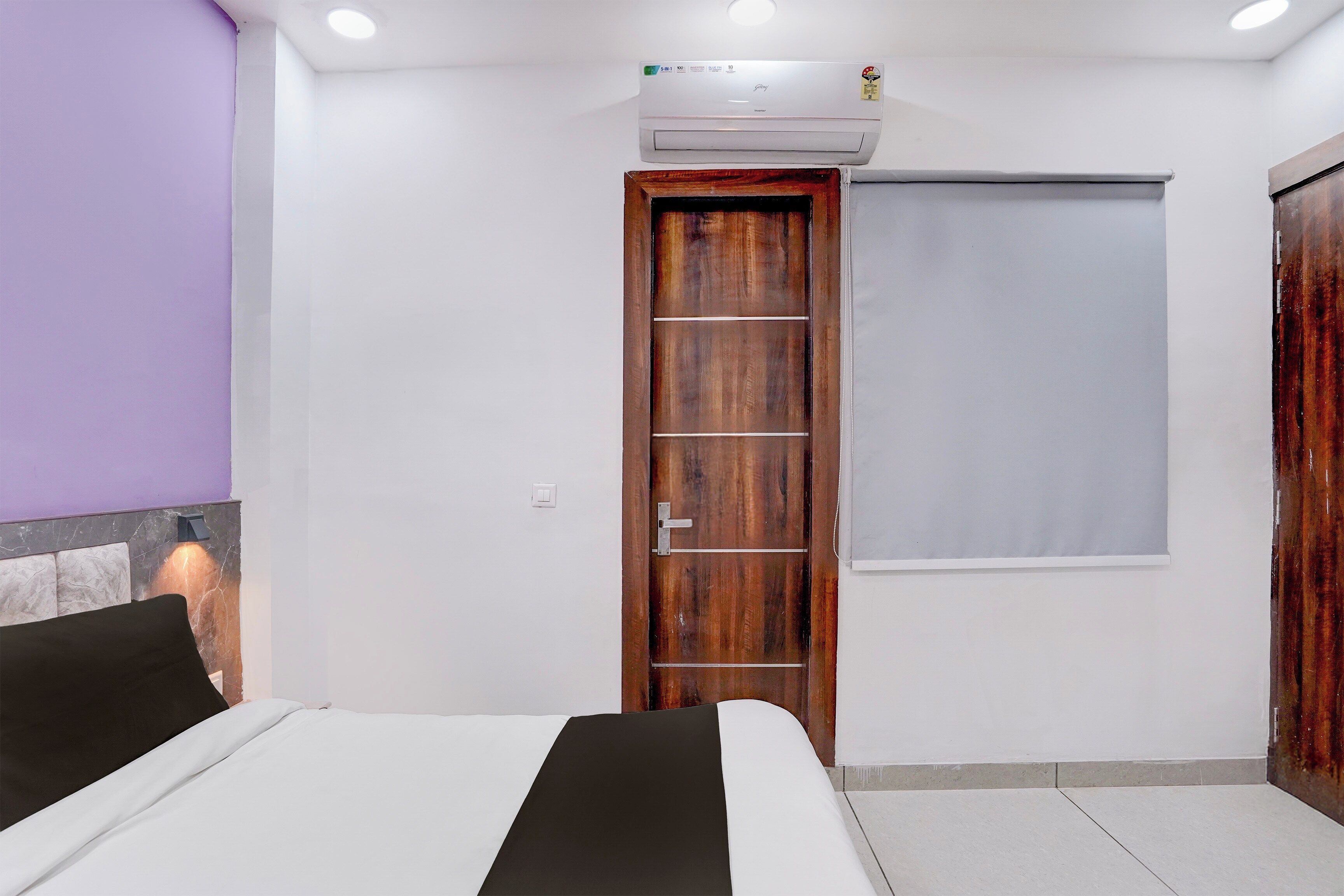 A bedroom with a bed, a wooden wardrobe, a door with a window, and an air conditioning unit.