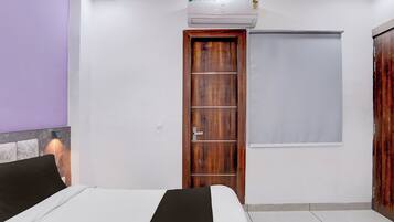 A bedroom with a bed, a wooden wardrobe, a door with a window, and an air conditioning unit.