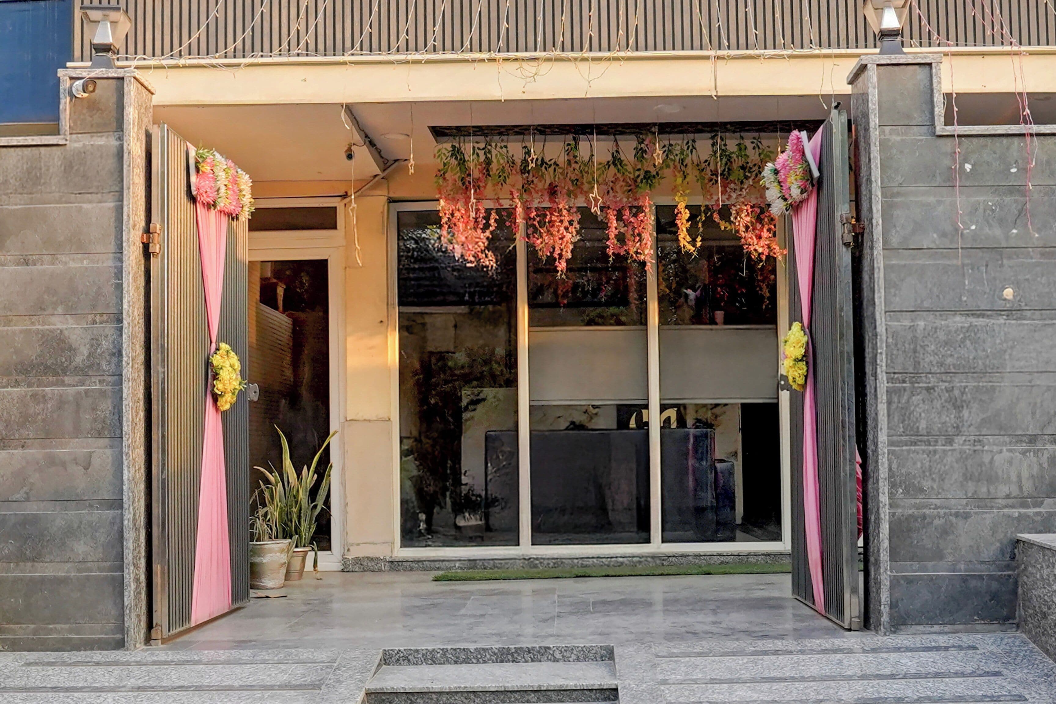 A building entrance with a glass door, pink curtains, and hanging floral decorations.