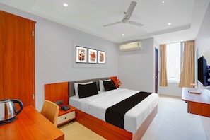 Ein Hotelzimmer mit Bett, Schreibtisch, Stuhl, Telefon, Wasserkocher, Deckenventilator, Klimaanlage und Fernseher.