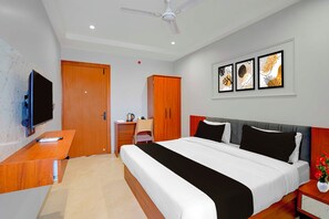 Ein Hotelzimmer mit Bett, Schreibtisch, Fernseher, Kleiderschrank und Deckenventilator.