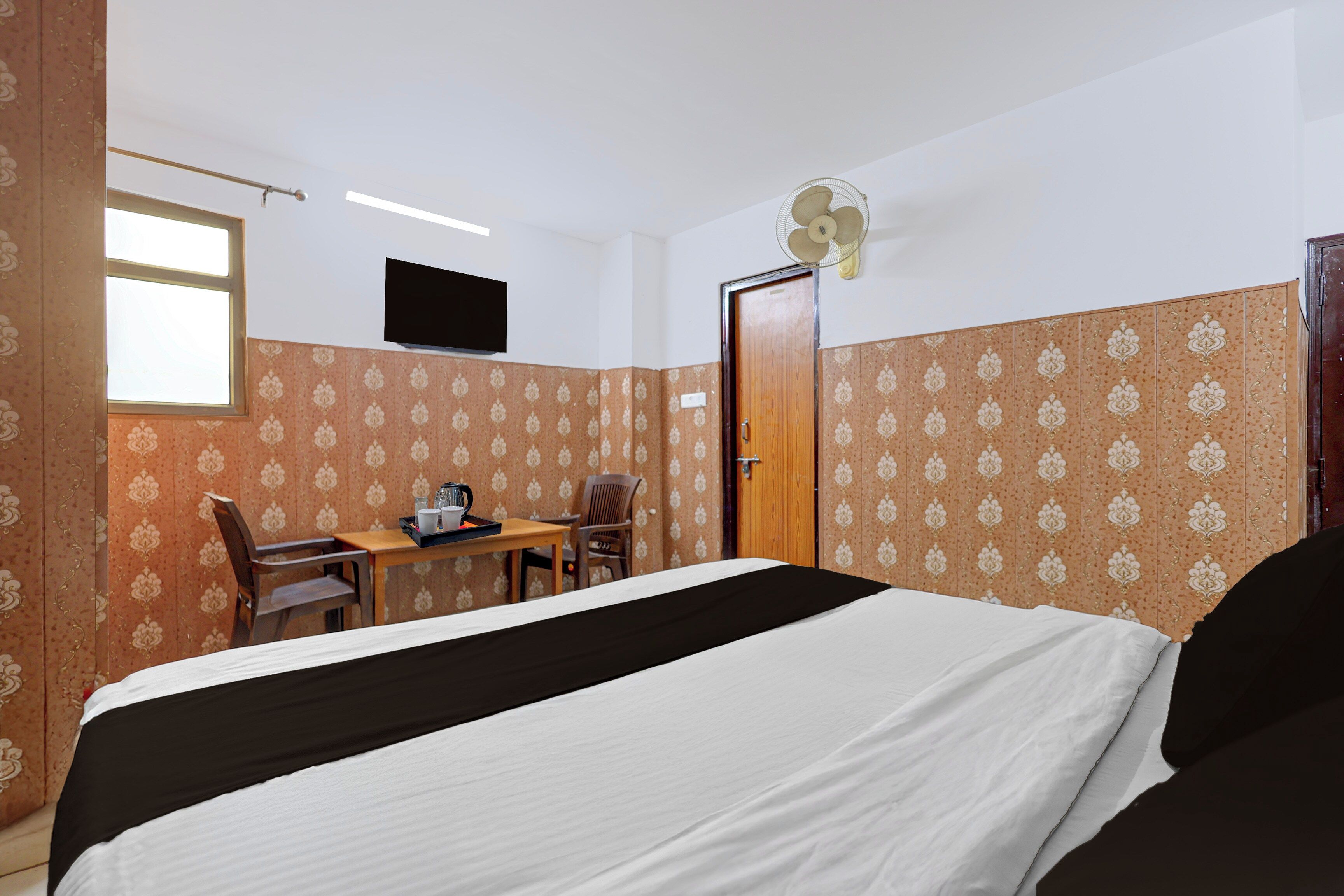 Ein Hotelzimmer mit einem Bett, einem Schreibtisch mit Stuhl, einem Fernseher und einer Tür.