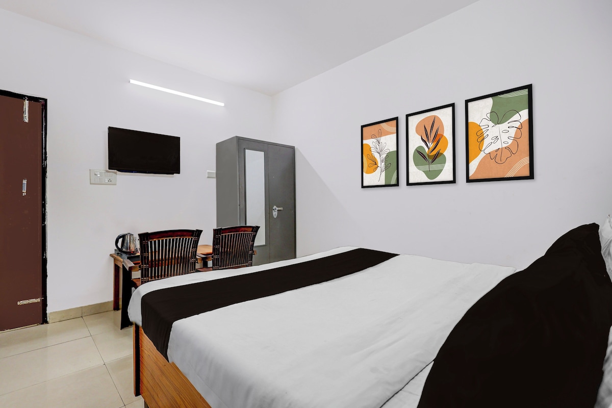 A hotel room with a bed, a desk with a chair, a television mounted on the wall, and three framed artworks.