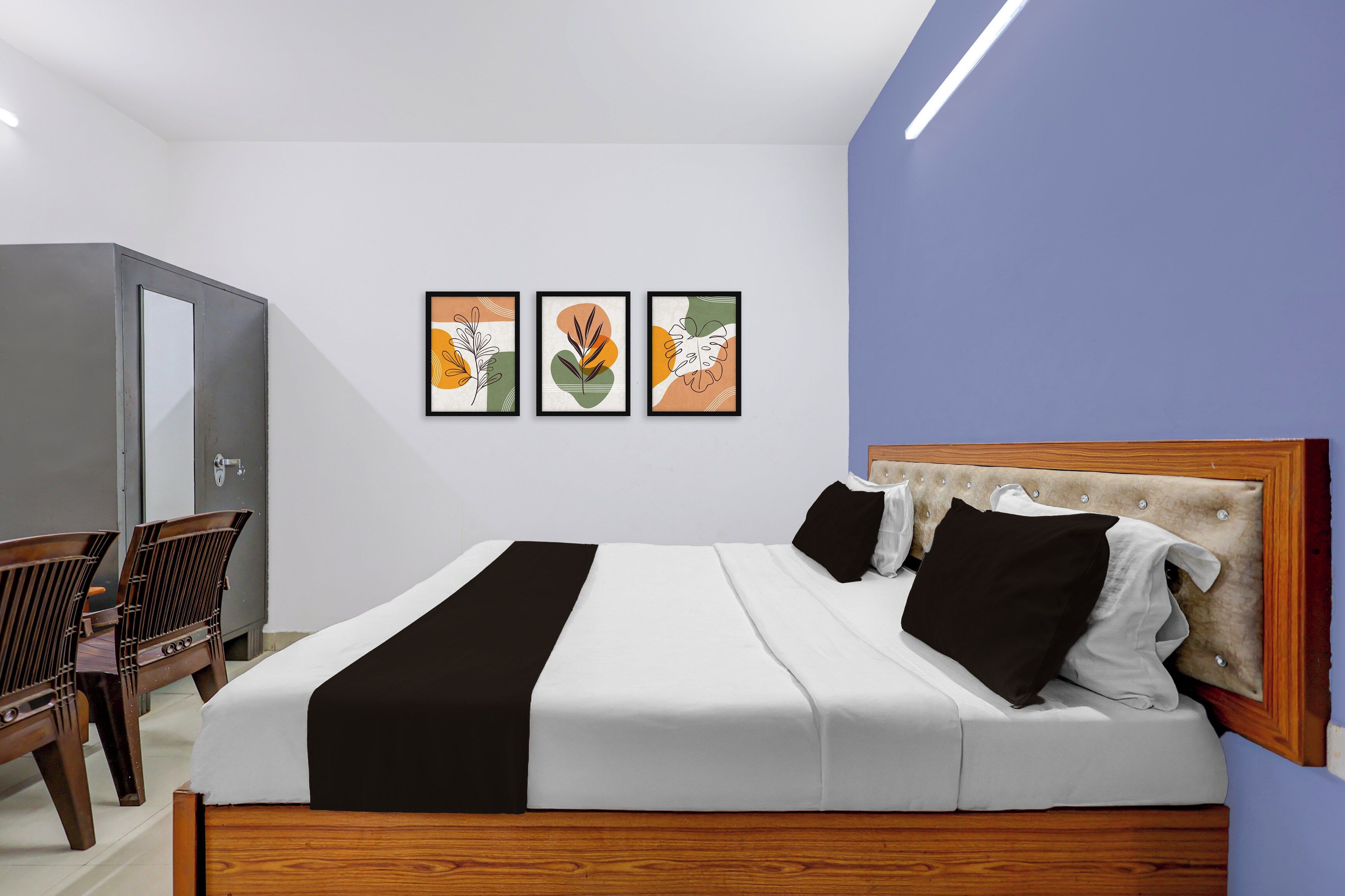 A modern bedroom with a bed, a wooden headboard, a desk, and a chair. There are three framed artworks on the wall.