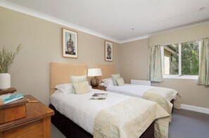 A hotel room with two beds, a bedside table with a lamp, a window with curtains, and two framed pictures on the wall. - The Allensford (Hexham)