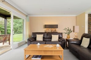 A modern living room with a brown leather sofa, a wooden coffee table, and a large window with a view of greenery. - The Allensford (Hexham)