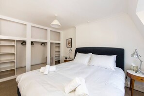 A neatly arranged bedroom with a large bed, white bedding, a black headboard, and a built-in wardrobe with multiple shelves and hanging space. - 2 Bed Apartment, Notting Hill (London)