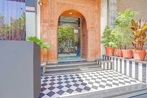 A hotel entrance with an ornate archway, checkered flooring, and potted plants.