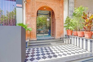A hotel entrance with an ornate archway, checkered flooring, and potted plants.