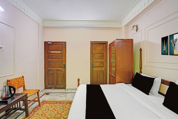 A hotel room with a bed, a chair, a table with a kettle, and two doors.