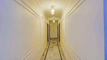 A hotel hallway with marble flooring, white walls, and a ceiling light fixture.