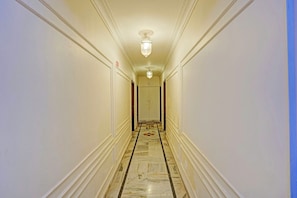 A hotel hallway with marble flooring, white walls, and a ceiling light fixture.