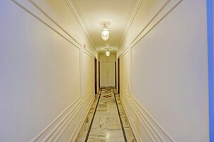 A hotel hallway with marble flooring, white walls, and a ceiling light fixture.