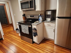 A kitchen with a stove, microwave, coffee maker, and refrigerator.