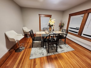 A dining area with a glass table, black chairs, a white chair, a rug, and a vase with flowers. - Blue siren nest (Ludlow)