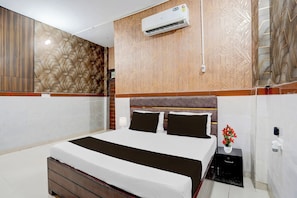 Una habitación de hotel con cama, aire acondicionado, mesita de noche y un jarrón con flores.