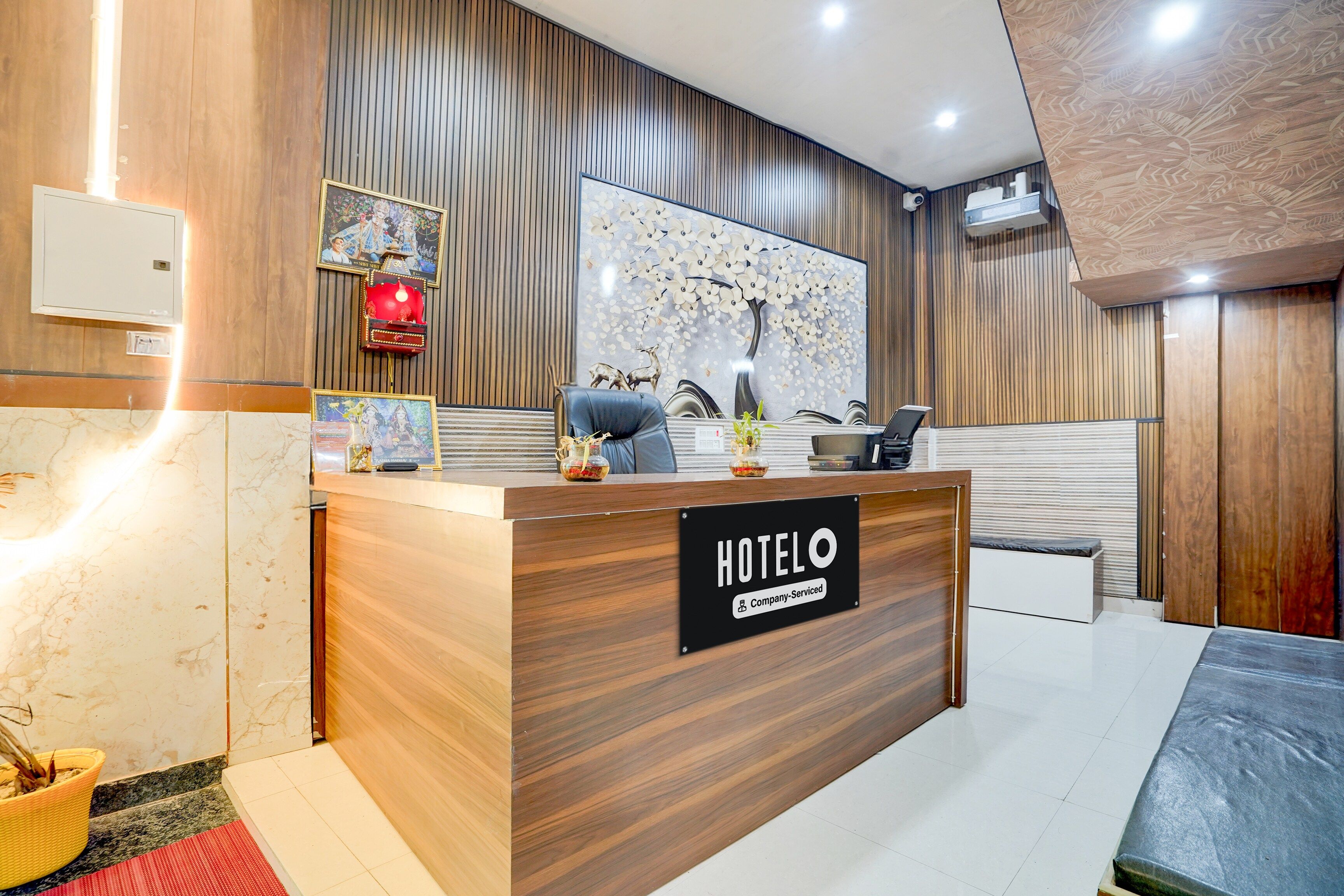 A hotel reception desk with a 'HOTELO' sign, a framed picture, and a decorative tree mural on the wall.