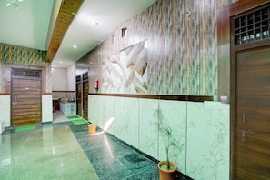 Una zona de recepción con pared de mármol, puerta de madera y un felpudo verde en el suelo.