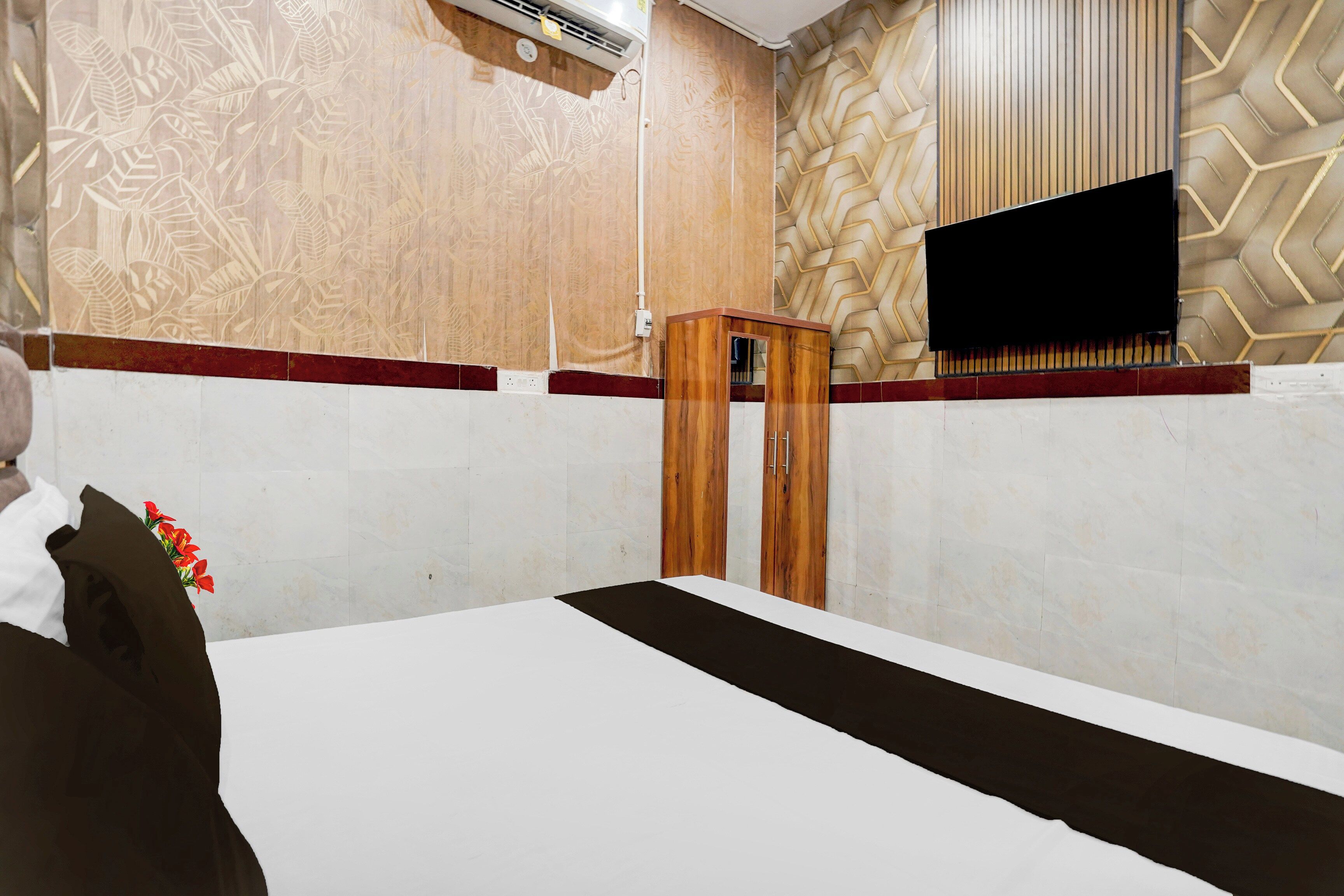 Habitación de hotel con cama, mesita de noche de madera, televisor montado en la pared y papel tapiz estampado.
