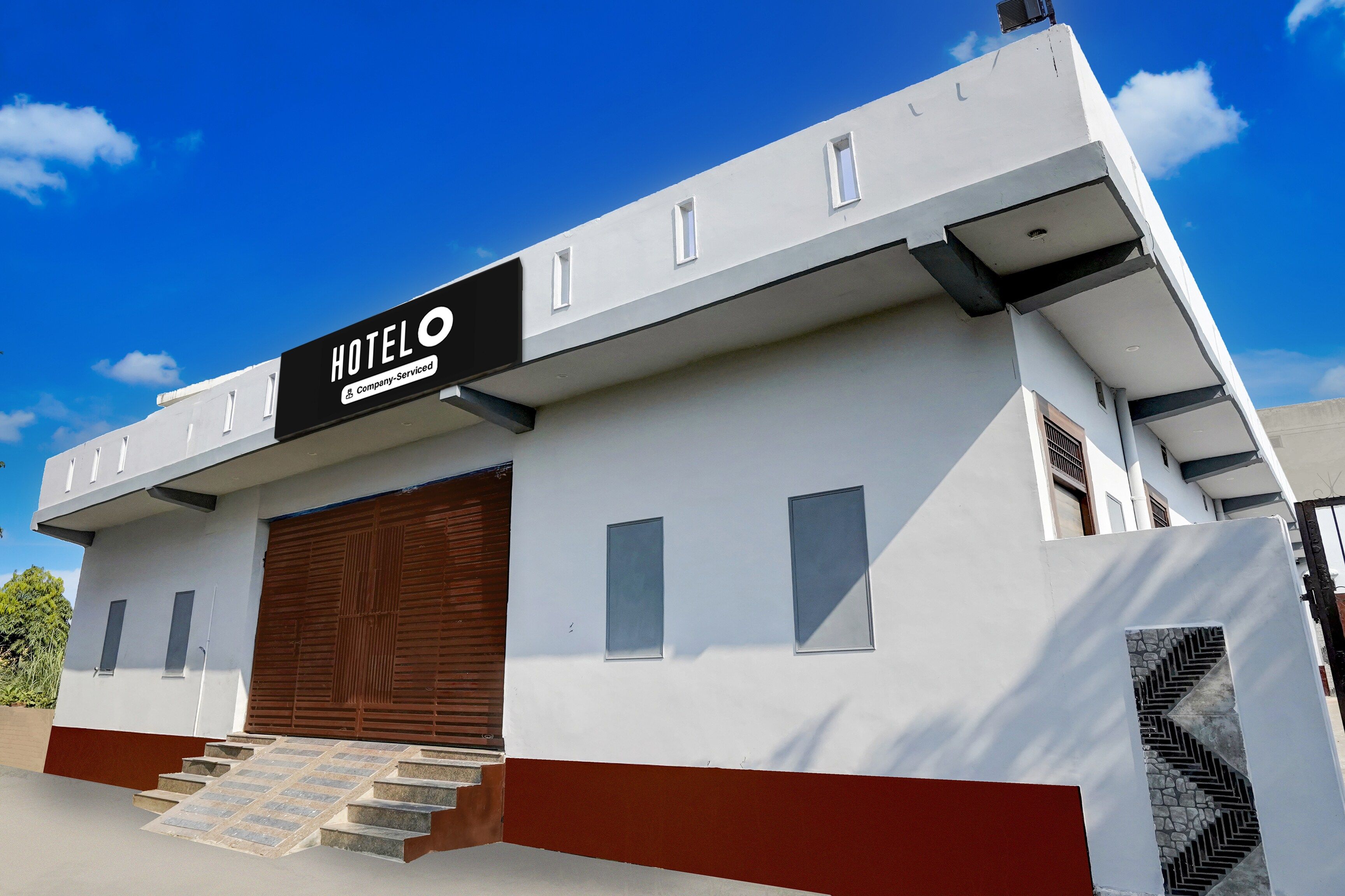 Um edifício moderno de hotel com um letreiro chamativo 'HOTEL', uma grande porta de garagem e uma escadaria que leva à entrada.