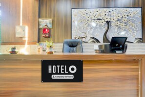 Mostrador de recepción de hotel con un cartel que indica servicio de empresa. Hay una foto en un marco en la pared, un mural decorativo de un árbol y una estatua de ciervo.