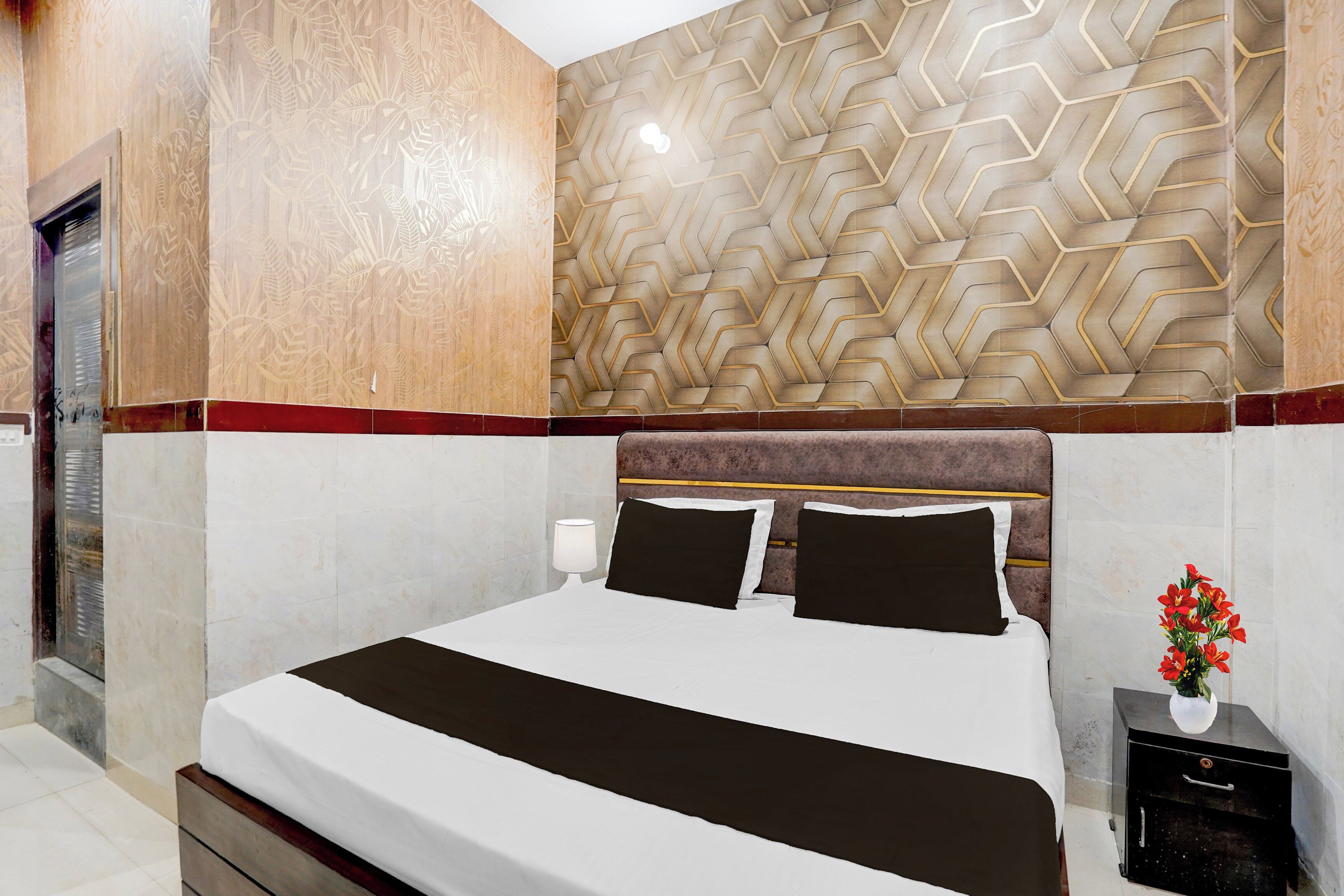 A hotel room with a bed, a nightstand, a lamp, and a wall with a geometric pattern.