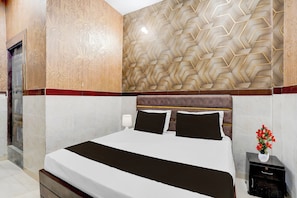 Quarto de hotel com cama, mesa de cabeceira, abajur e parede com padrão geométrico.