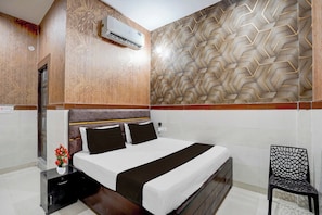 Quarto de hotel com cama, uma cadeira, mesa de cabeceira e ar condicionado.