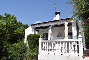 A white building with a balcony, surrounded by greenery.